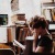 woman, surrounded by books, sits and reads in front of a picture window